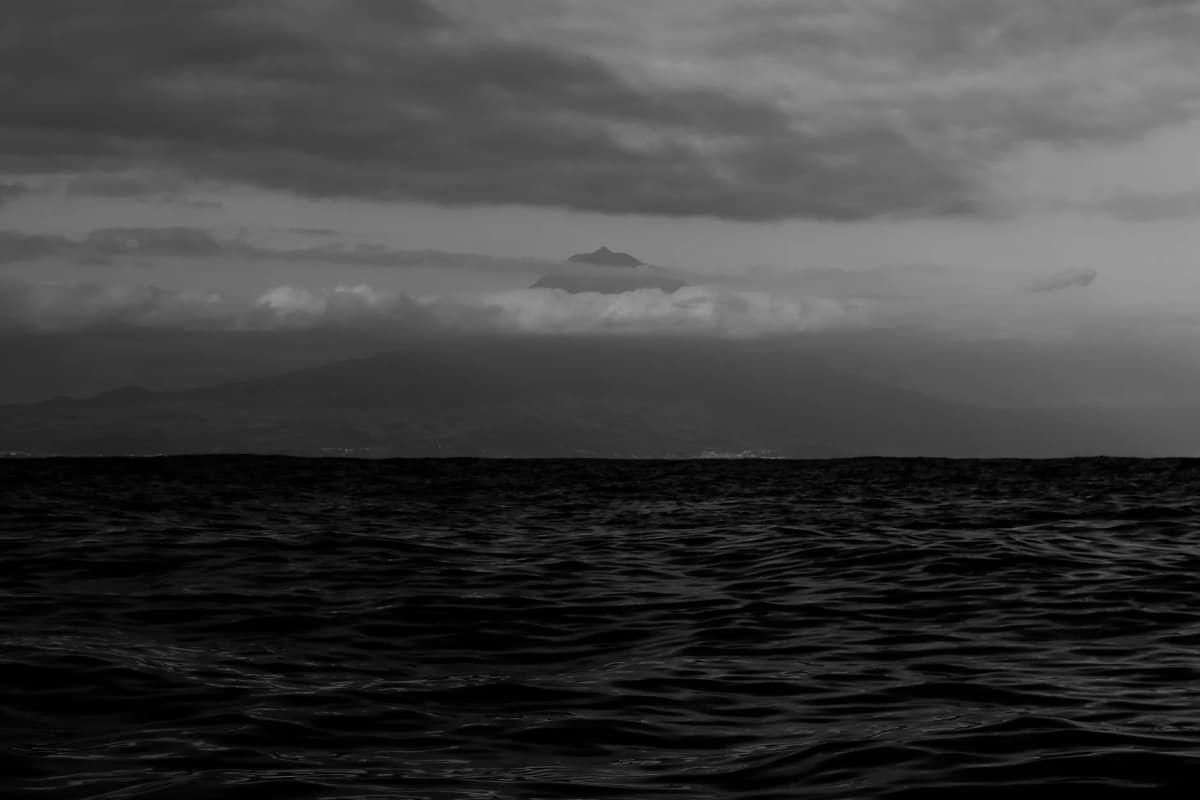 Moody black-and-white seascape with Mount Pico under cloudy skies in Azores, Portugal.